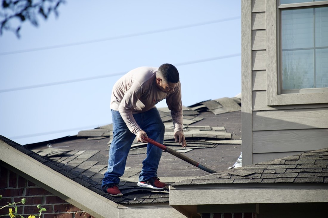 A Ridgeline Roofing crew member removing old shingles during a roof tear-off